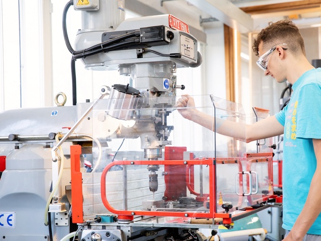 Student shown using a pillar drill with safety measures in place